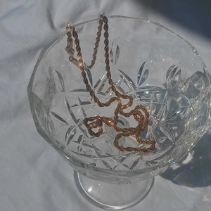 Golden titanium steel twisted rope chain necklace shown in a crystal glass for layering