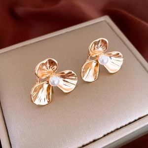 Detailed close-up of golden petal stud earrings with white pearls on premium leather