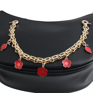 Golden bag chain strap with red flower charms and lobster clasps on leather background