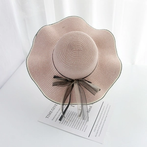 Pink wavy brim straw hat featuring black lace bow and checkered trim in an elegant setting