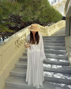 Detail of white V-neck dress with ruffles, straw bag, and hat in a resort setting
