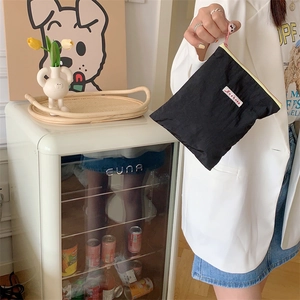 Portable black fabric cosmetics pouch with a zip, held in a cozy home setting