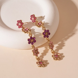 Détail macro de boucles d'oreilles longues dorées avec cristaux de fleurs roses