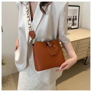 Detail of brown lychee leather bucket bag featuring a cream FASHION letter strap