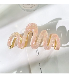 Detail of pink marble acetate shark hair clip with wavy gold metal frame on white surface