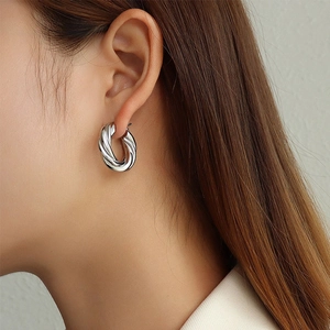 Close-up of twisted croissant earrings in silver finish worn by a model in soft light