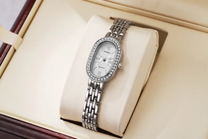 Gros plan d'une montre ovale argentée sertie de strass sur un coussin en velours