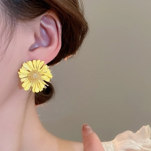 Close-up of yellow raffia daisy stud earring with 3D petals worn by a model