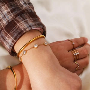 Close-up of gold geometric heart zircon bracelet and bangles layered on a model's wrist