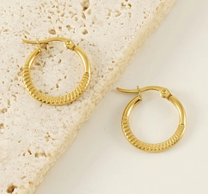 Detail shot of golden hoop earrings with radial striped texture on a textured stone plate