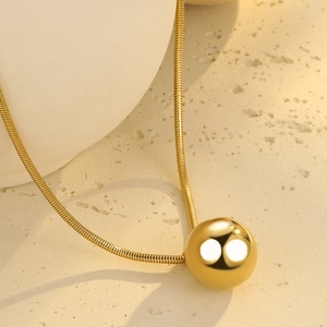 Macro shot of polished gold ball pendant on a sleek snake chain necklace for women