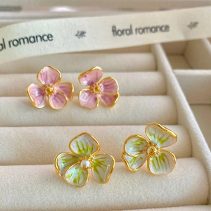 Vue macro de boucles d'oreilles fleurs en émail rose et vert sur ruban de soie