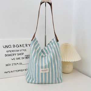 Detail of blue striped canvas tote bag showing the branded studio label and brown strap