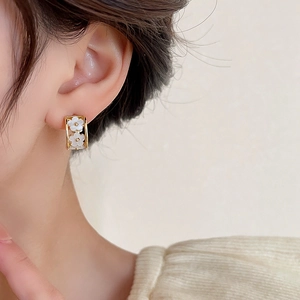 Close-up of golden C-shaped flower earrings with white petals on a female ear