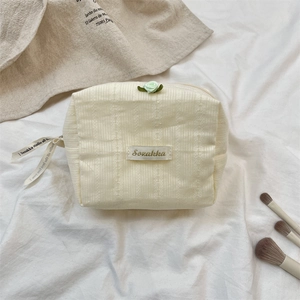Detail of beige corduroy makeup bag with green rose accent and printed ribbon puller
