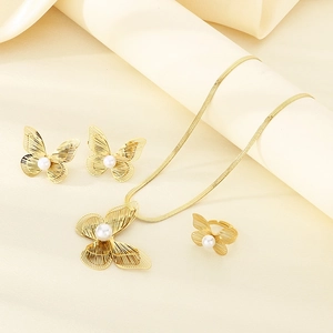 Detailed set of gold butterfly jewelry with pearls on elegant beige fabric background