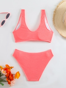 Flat lay of coral pink textured bikini set with high-waisted bottom and summer beach accessories