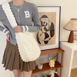 Detail of a cream white bubble textured crossbody bag worn by a model in a cozy home setting