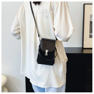 Rear view of a model wearing a small black PU leather crossbody bag with silver buckle