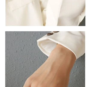 Detailed close-up of textured white blazer fabric with elegant cuff buttons and stitching