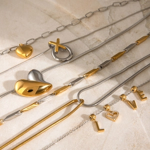 Elegant gold and silver tone heart and letter pendant necklaces on marble surface