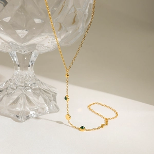 Collier en acier doré avec zircons verts suspendu sur un récipient en verre