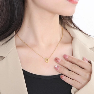 Close-up of a minimalist gold collar necklace with a sleek oval number 0 pendant on a model