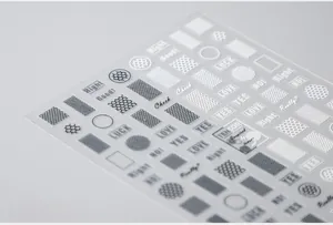 Detailed close-up of 5D nail art stickers with black and white geometric patterns and text