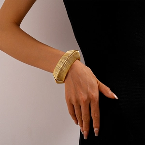 Detail of a bold gold wire-wrapped wide cuff bracelet on a woman's wrist with high-end texture
