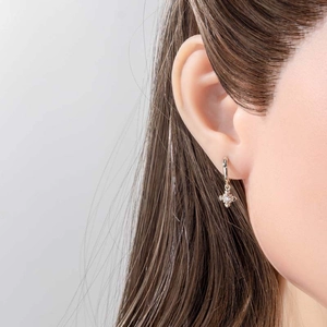 Gold huggie hoop earrings with sparkling star cross pendant worn by model on grey background
