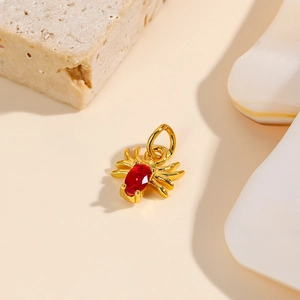 Detail of a golden spider pendant with a red gemstone inset on a beige stone base