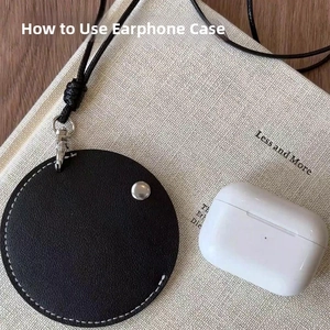 Close-up of black round leather earphone case with white stitching and silver snap
