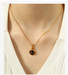 Detail of a vintage 18K gold snake chain necklace with a round turquoise pendant on a model