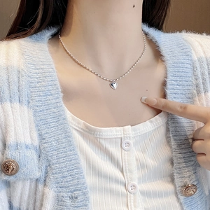 Detailed view of polished silver heart pendant necklace worn on a blue striped sweater