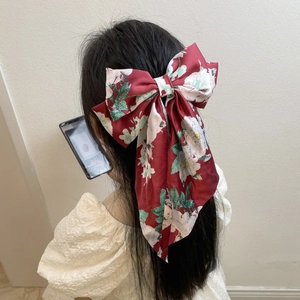 Detail of a large red floral bow hairpin with long ribbons worn on a model's hair