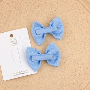 Detail of two light blue bow hair clips with textured fabric on a natural cork background