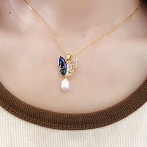 Detailed view of a golden butterfly pendant featuring white pearl and zircon on model neck