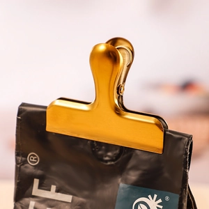 Golden brushed stainless steel bag clip sealing a coffee pouch with a secure grip