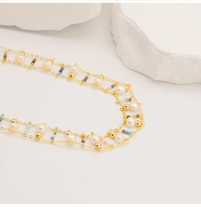 Close-up of double-layer gold necklace with natural pearls and colorful beads on white stones