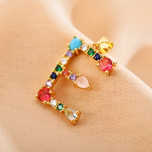Macro shot of letter F gold pendant encrusted with colorful zircons and mixed gemstones
