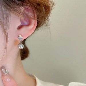 Close-up of elegant four-leaf clover stud earrings with grey pearl drop on a model