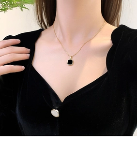 Close-up of a 18k gold-plated necklace with a black square pendant on a woman's collarbone