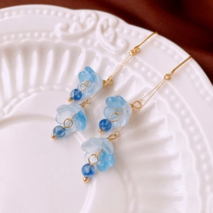 Détail des boucles d'oreilles fleurs en verre bleu clair avec glands papillons sur porcelaine