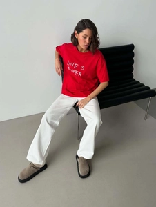 Oversized red T-shirt with white Love Is Power print on model sitting on a bench