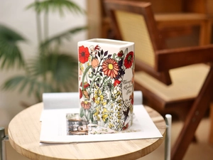 Detail of book-shaped ceramic vase featuring Lewis Carroll floral art on wooden table