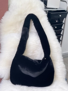 Detail of soft black faux fur shoulder bag on plush white texture background