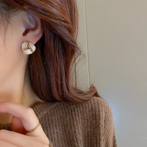Gros plan d'une boucle d'oreille nœud géométrique blanc crème avec cadre doré sur modèle