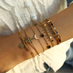Ensemble de bracelets superposés dorés avec breloques croix et lune portés au poignet