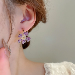 Close-up of purple crystal flower earring with gold setting worn on a model ear