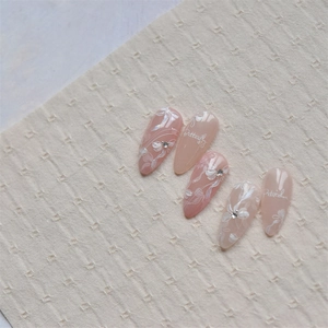 Macro detail of nude pink almond press-on nails with white floral art and rhinestones
